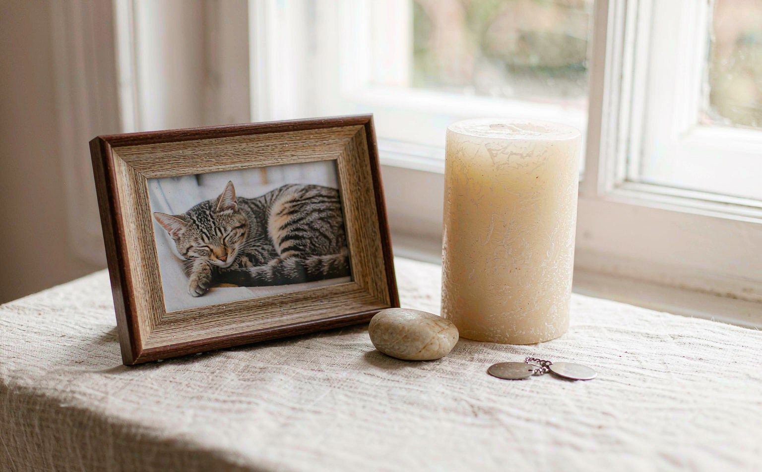 A small memorial keepsake arrangement on a linen surface: a framed pet photo, a candle and an engraved photo keychain