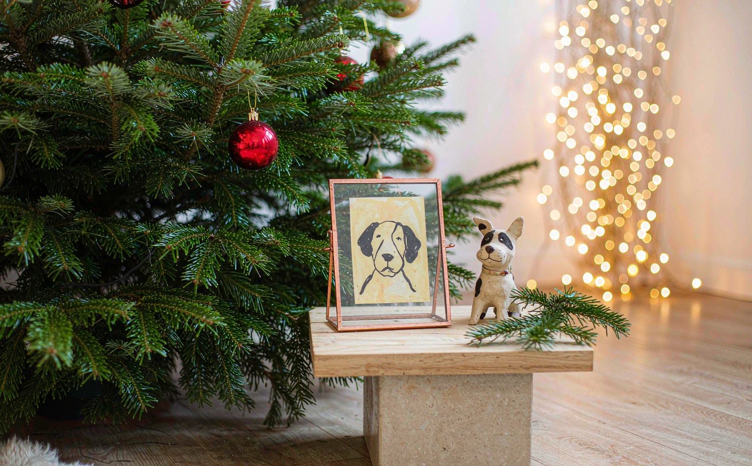 A handmade clay dog figurine and a glass pet portrait beside a Christmas tree &mdash; pet memorial Christmas gifts