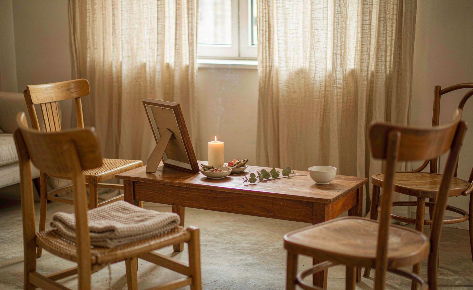 A quiet living room set up for a home pet memorial service &mdash; four chairs, a candle, a framed portrait and dried flowers
