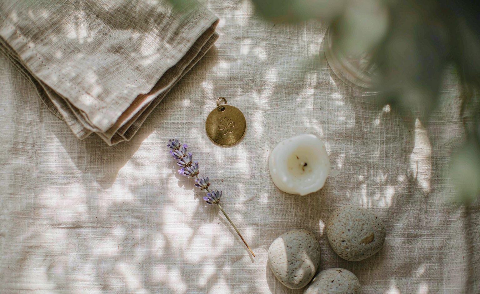 A small brass pet tag, river stones, dried lavender and a burnt candle on linen &mdash; simple keepsakes for a pet memorial ceremony